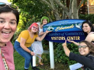 4 youth pointing at the Welcome to Edmonds sign while young woman in front takes a selfie